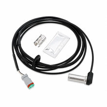 A black coiled cable assembly with a gray and green connector on one end and a silver metal cylindrical component on the other, shown with a small silver clip and a sealed plastic packet on a white background.