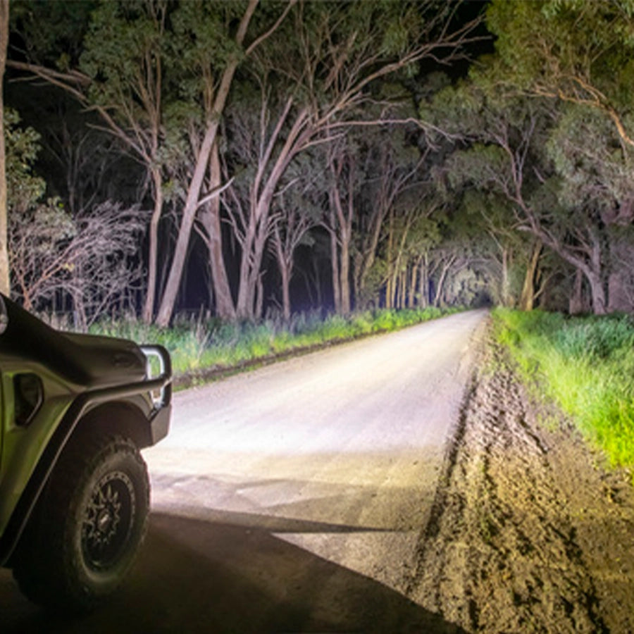 Car driving on a forest road at night with headlights illuminating the path.