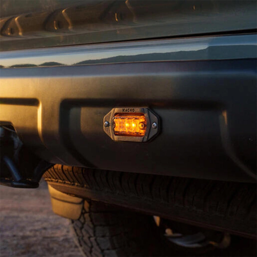 Close-up of a vehicle's front bumper with a visible light, set against a blurred natural background.
