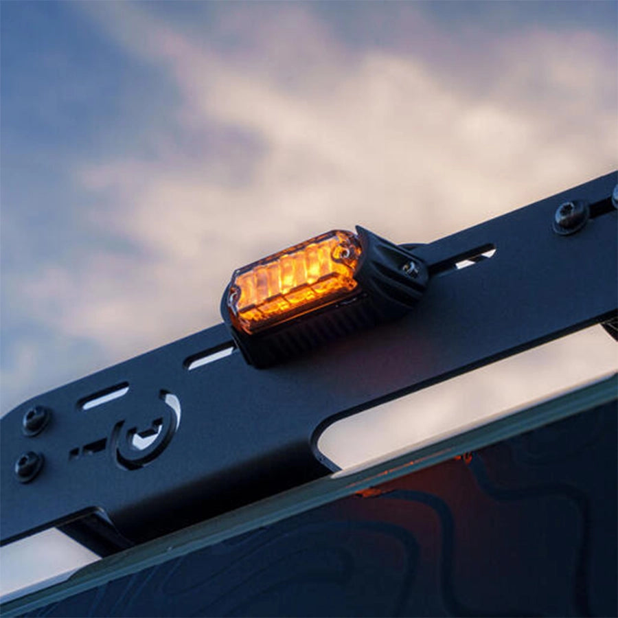 Amber LED light on a vehicle roof rack with a cloudy sky background