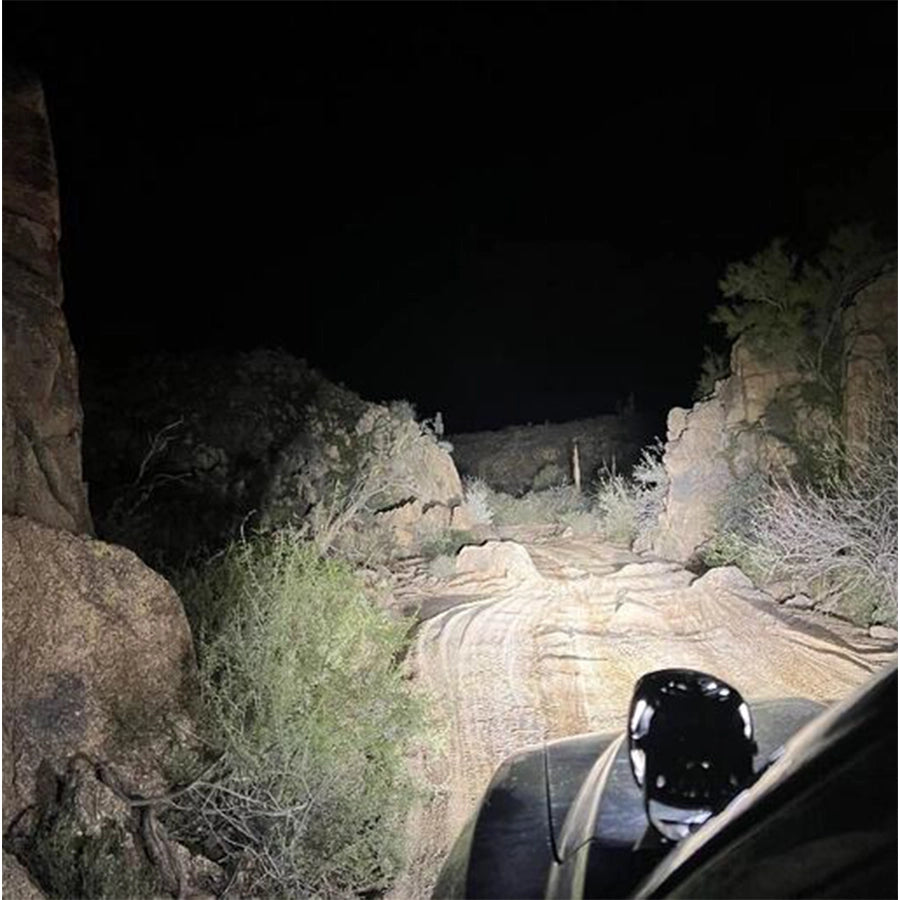 Car driving on a rocky desert road at night with headlights illuminating the path.