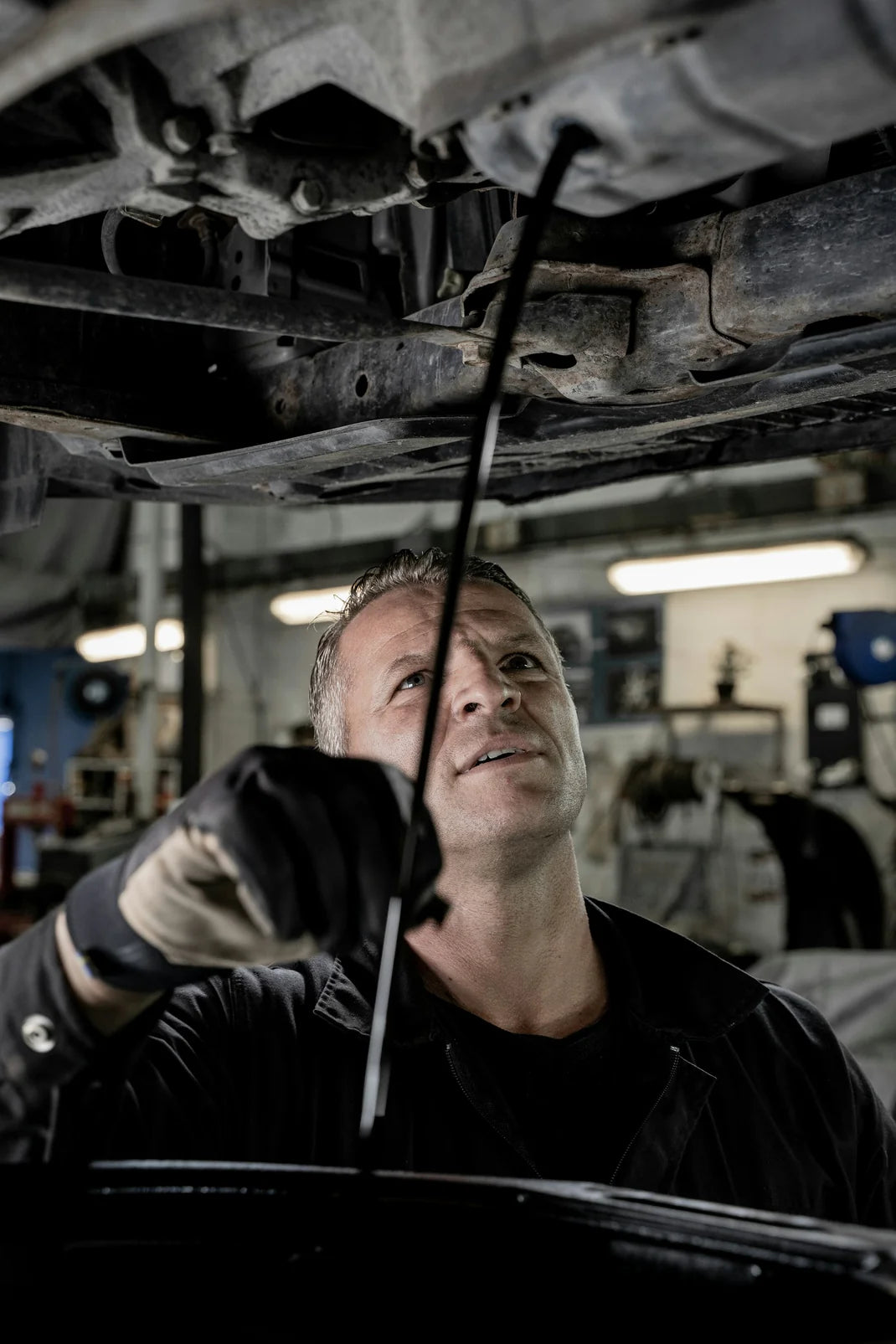 Mechanic checking oil levels under a vehicle in a garage.